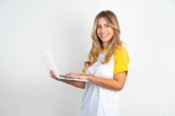 Adorável jovem mulher bonita vestindo futebol camiseta sobre fundo branco segurando dispositivo moderno - Foto, Imagem