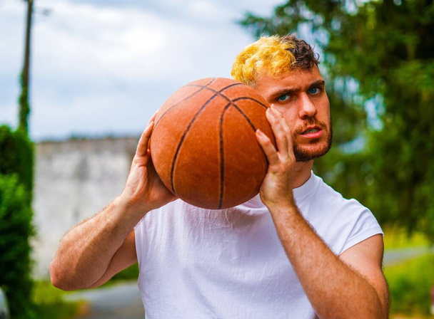 Hispanic basketball player posing with a basket ball grabbing it with both hands and trying to intimidate with his face - Foto, Bild
