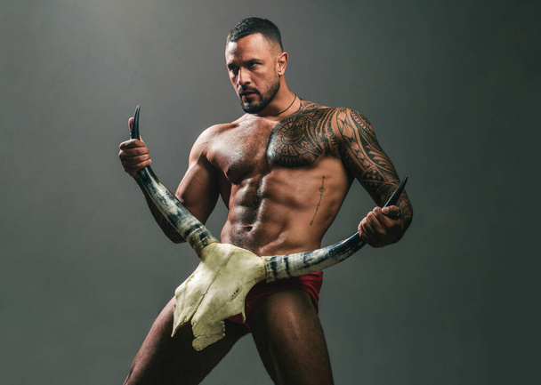 Desire is the energy force. Sexy latino man showing his sexual desire and attraction. Muscular hispanic man with fit body holding skull and horns. Attractive power and desire force. Desire concept. - 写真・画像