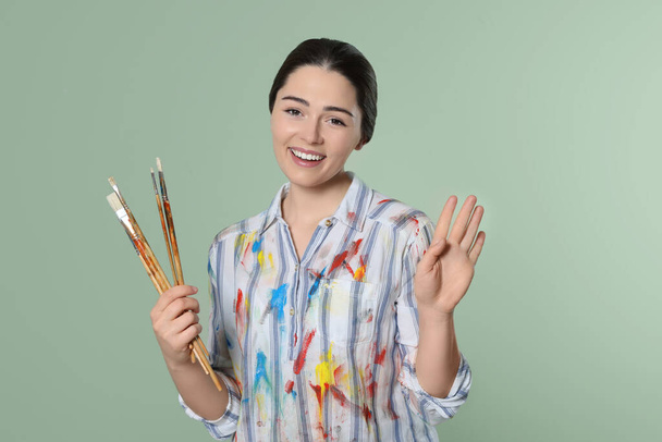 Woman with paintbrushes on pale green background. Young artist - Fotó, kép
