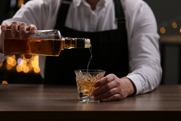 Bartender pouring whiskey from bottle into glass at bar counter indoors, closeup - Foto, afbeelding