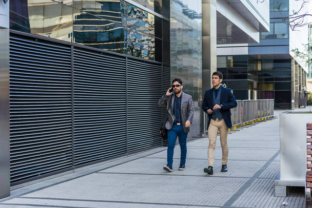 Two business colleagues are walking on the street. One of them is talking on the cell phone. - Fotoğraf, Görsel