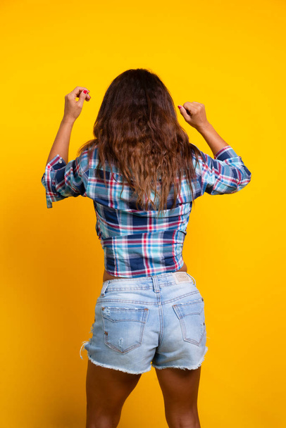 Woman dressed in character with pants and checkered shirt dancing Forro. Sao Joao party. June celebration. Isolated on yellow background. - 写真・画像