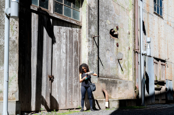 Woman drinking mate while standing outside an abandoned factory. Travel concept. - Photo, image