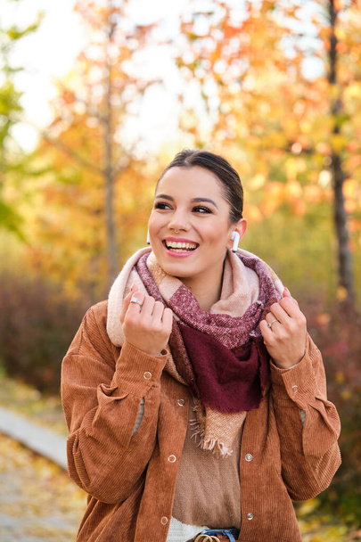 Caucasian young woman listening music with earphones smiling in autumn. - Photo, Image