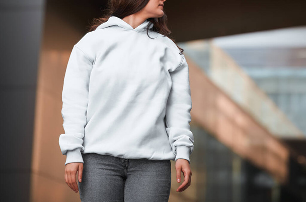 Een jong meisje draagt een witte hoodie. Geen logo basic sportkleding. Mockup sweatshirt met lange mouwen. - Foto, afbeelding