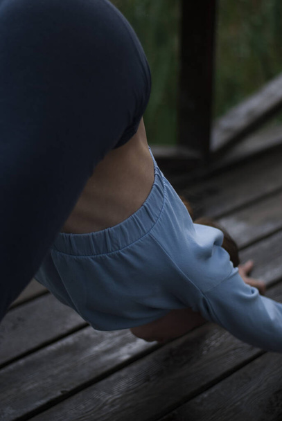 Vue d'une fille avec un corps athlétique en costume de gym bleu fait des exercices dans le parc en temps nuageux pluvieux weathe - Photo, image