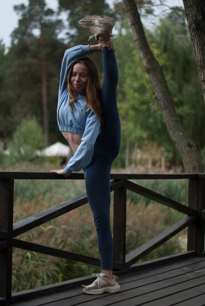 View of young girl with athletic body is doing acrobatics exercises in rainy weather in the park - Photo, Image