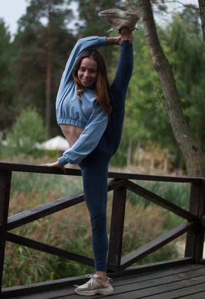 View on young girl with athletic body is doing acrobatics exercises in rainy weather in the park - Φωτογραφία, εικόνα
