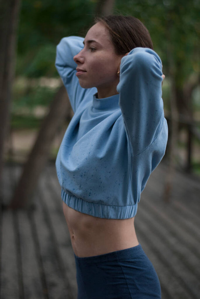 Pohled na portrét dívky v modrém tělocvičně v parku za oblačného počasí - Fotografie, Obrázek