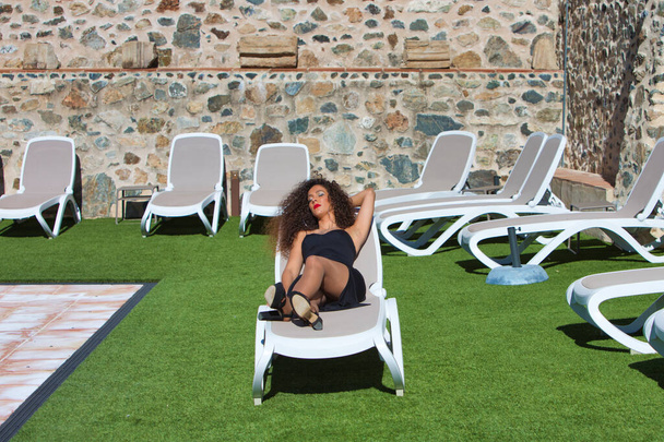 Belle femme brune vêtue d'un costume d'été noir, relaxante sur une chaise longue bronzant au bord de la piscine sur la terrasse d'un hôtel de luxe. Femme est en vacances en Andalousie, Espagne. - Photo, image