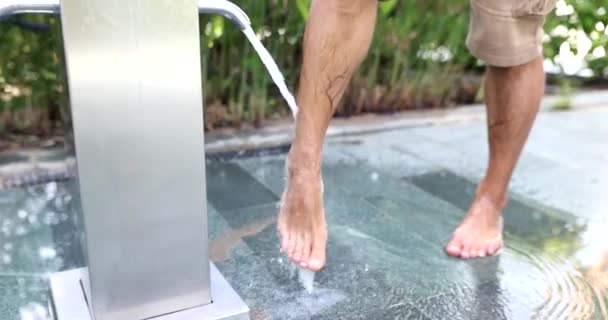 Az ember lábat mos a zuhany alatt a tenger partján. Higiénia és lábmosás medencével - Felvétel, videó
