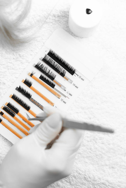 This photo offers a glimpse into the lashmakers eyelash extension skill. Beauticulo tweezers take an artificial eyelash and prepares to apply on the eyelids. Close-up view from above. High quality - Photo, Image