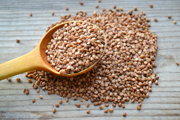 Buckwheat grains with an old big spoon on wooden table - Photo, Image