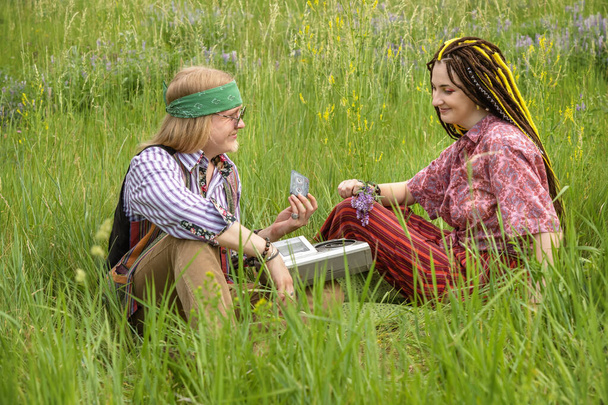 Hippie ragazzo offre la sua ragazza per ascoltare una cassetta audio su un registratore di cassette vintage mentre seduto nell'erba in una radura foresta - Foto, immagini
