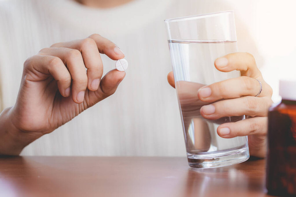La mano de la mujer que toma la píldora de la medicina y el agua potable con el frasco marrón en la mesa para el concepto de salud. - Foto, imagen