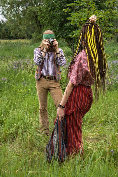 Hippi adam ormanda eski bir kamerayla rastalı bir kızın fotoğraflarını çekiyor. - Fotoğraf, Görsel