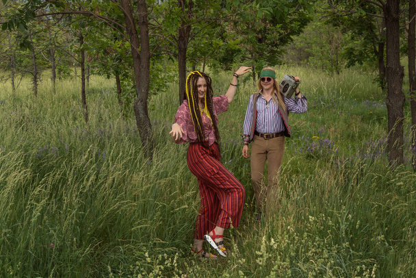 Un paio di giovani in stile hippie nella foresta. Una ragazza sta ballando, un ragazzo sta portando un nastro retrò cassetta - Foto, immagini