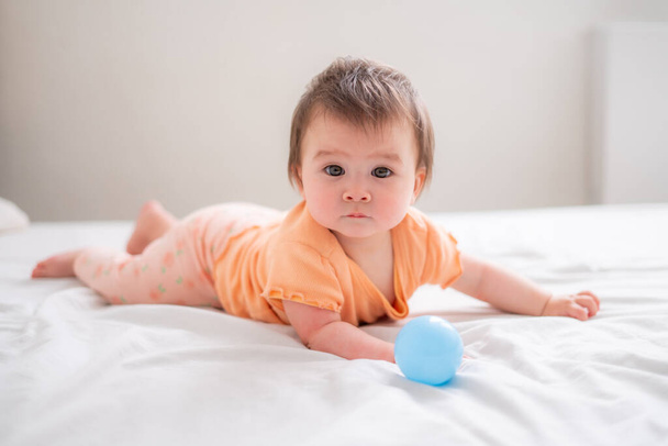 lifestyle home portrait of happy and beautiful 8 months old baby girl mixed race Asian Caucasian playing with ball cheerful on bed and exploring the surroundings curious  - Foto, afbeelding