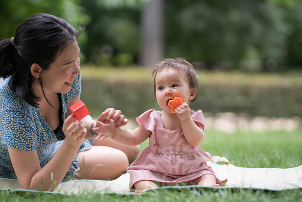 estilo de vida al aire libre retrato de la madre y la hija - joven mujer china asiática feliz y dulce jugando con su bebé de 8 meses en la hierba en el parque de la ciudad - Foto, imagen