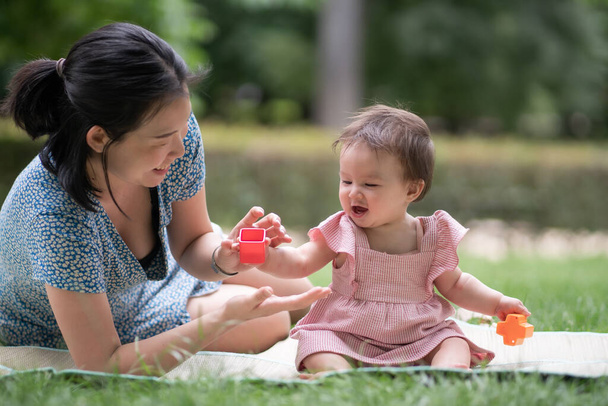 outdoors lifestyle portrait of mother and daughter - young happy and sweet Asian Korean woman playing with her 8 months baby girl on grass at city park - Foto, imagen