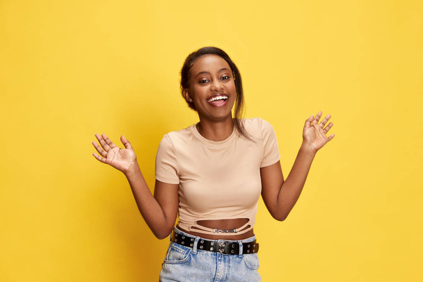 Portrait of beautiful, happy, young african girl in casual clothes posing with smile and laugh against yellow studio background. Concept of lifestyle, human emotions, fashion, beauty, ad - Фото, зображення