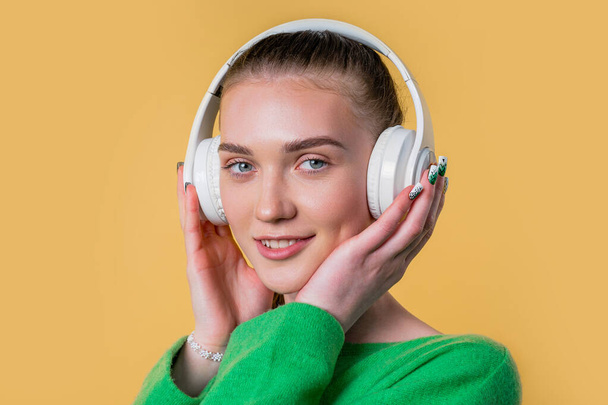 Positive woman listening music, enjoying with headphones on yellow studio background. Radio, wireless modern sound technology, online player. High quality - Фото, изображение