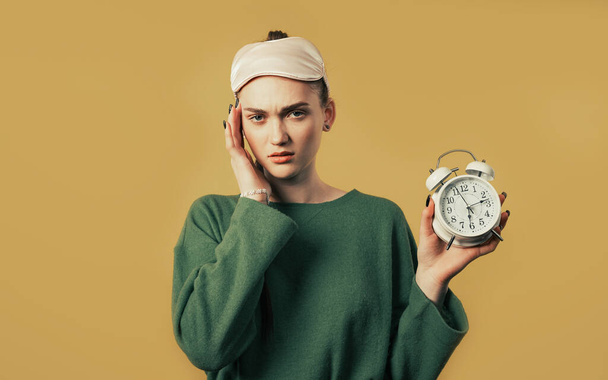 Woken up by alarm clock sleepy woman holding it in hand. Yellow background. Early 6 o'clock in morning. Lazy lady didn't get enough sleep, concept of passing time. High quality photo  - Photo, image
