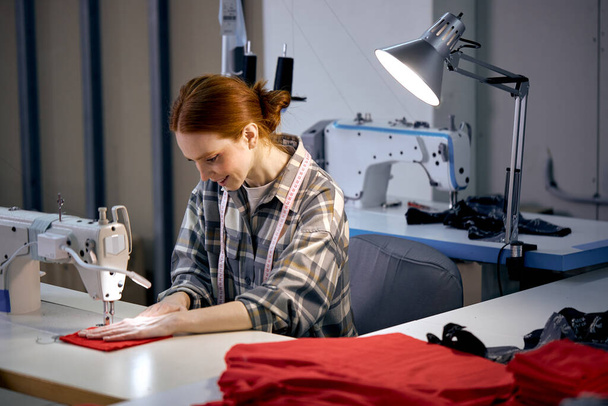 Textile cloth factory working process tailoring modern clothes, young beautiful caucasian woman at work, engaged in tailoring using modern sewing machine. dressmaker enjoy sewing, tailoring - Φωτογραφία, εικόνα