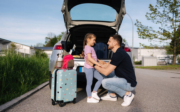 Tata i jego córka stoją przy otwartym bagażniku samochodu i przygotowują się do podróży, podczas gdy mama włącza alarm. Wysokiej jakości zdjęcie - Zdjęcie, obraz