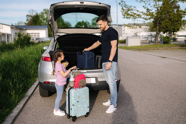Padre aiutare figlia caricamento al bagagliaio con bagagli prima di viaggiare mentre la mamma fa i bagagli. Foto di alta qualità - Foto, immagini
