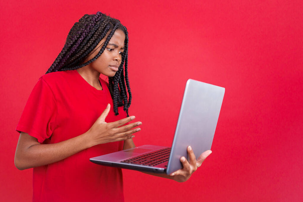 Afrikaanse vrouw met een probleem met een laptop in de studio met rode achtergrond - Foto, afbeelding