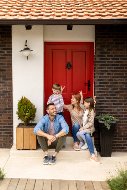 Rodina s matkou, otcem, synem a dcerou sedí venku na schodech na verandě cihlového domu - Fotografie, Obrázek