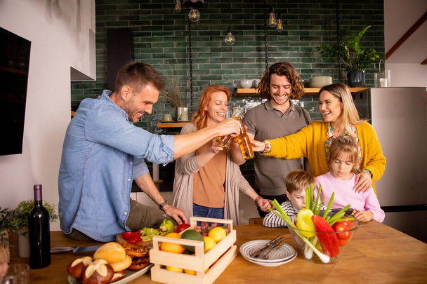 Duas famílias felizes brindam com cidra enquanto preparam o jantar na cozinha - Foto, Imagem