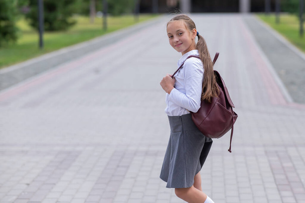 Portrait of caucasian schoolgirl in uniform and with backpack outdoors - 写真・画像