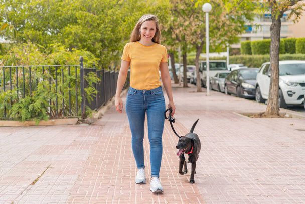 Young blonde woman with her adorable black dog at outdoors - Photo, Image