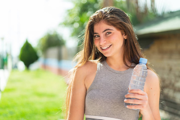 Young pretty caucasian woman with a bottle of water at outdoors smiling a lot - Фото, зображення