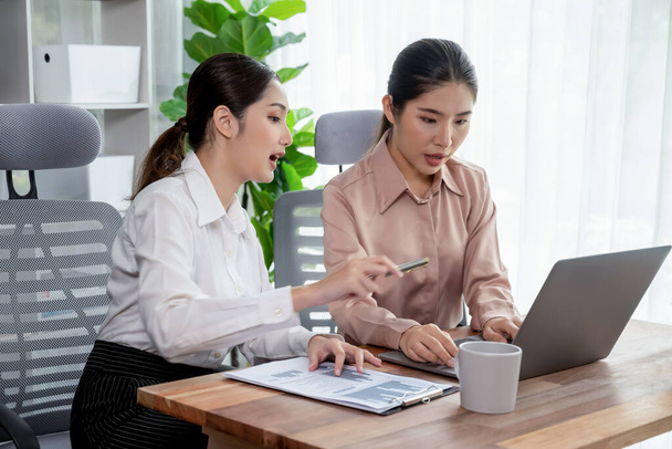 Two young office lady colleagues collaborating in modern office workspace, engaging in discussion and working together on laptop, showcasing their professionalism as modern office worker. Enthusiastic - Фото, зображення