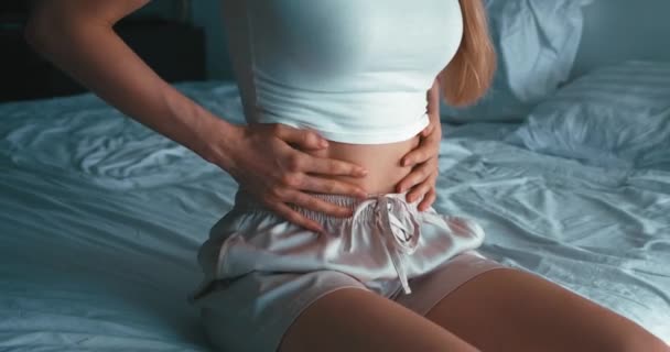 Vrouw met pijnlijke maagpijn zittend op bed in de slaapkamer. Zieke blanke vrouw die lijdt aan sterke buikpijn. Maagpijn bij menstruatie. - Video