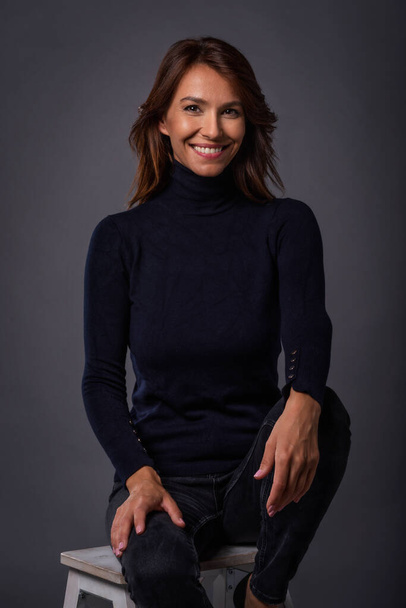 Studio portrait of a beautiful middle-aged woman looking at the camera. Attractive long haired female wearing black sweater and cheerful smiling against isolated background. - Fotoğraf, Görsel