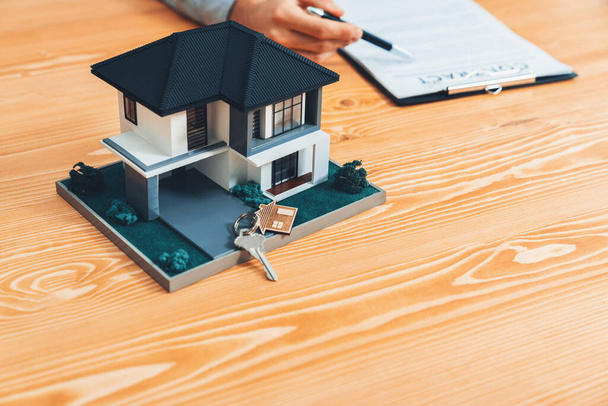 House model is displayed on wooden meeting table with in the blurred background of real estate agent and client discuss terms and conditions of house loan or rental lease contract. Entity - Foto, Imagem