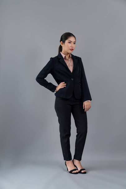 Full body length image of confident young businesswoman stands on isolated background, posing in formal black suit. Office lady or manager with smart and professional appearance. Enthusiastic - Fotografie, Obrázek