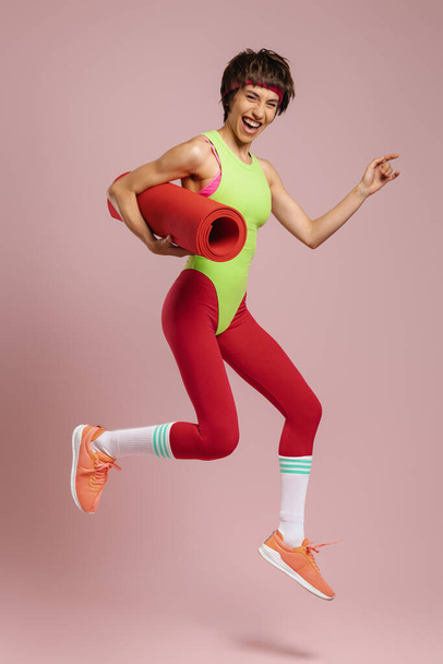 Mujer en forma feliz en ropa deportiva de estilo retro saltando sobre fondo amarillo - Foto, Imagen