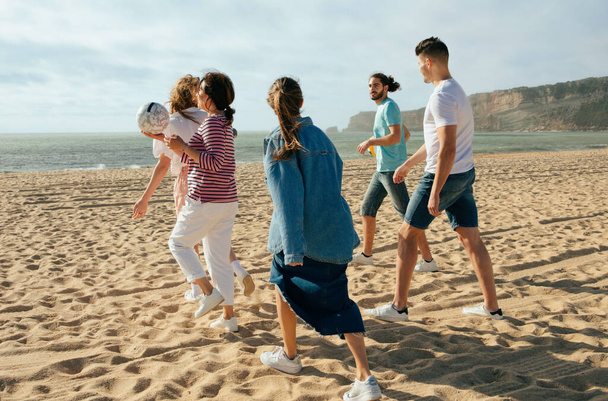 Satisfecho millennial árabe y caucásico personas en casual con bolas se divierten, ir a jugar juego activo en la playa en fin de semana, al aire libre. Vacaciones y caminar juntos, anuncio y oferta, picnic con amigos - Foto, Imagen