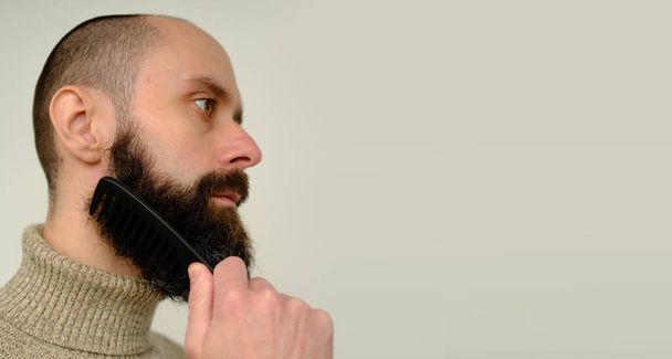 close-up of male face, young bearded and mustachioed man, guy with 25 - 30 years combs his thick beard, concept of mustache and beard stubble care products, hairline hygiene on lower part of face - Foto, Imagem