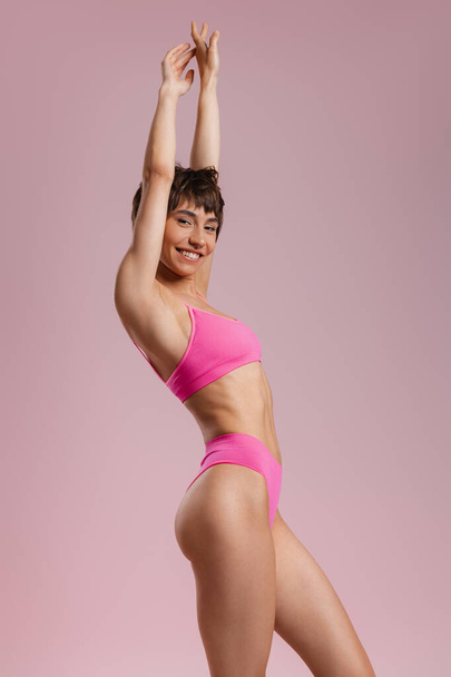 Happy young fit woman in underwear keeping arms outstretched against colored background - Foto, imagen