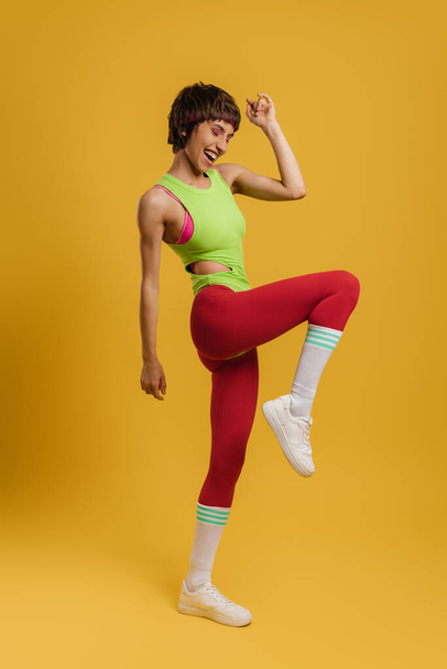 Full length of excited fit woman in retro styled sports clothing exercising against yellow background - Фото, изображение