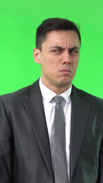 Unpleasant male with black hair in formal suit frowning and feeling aversion while standing isolated on chroma key in light studio - Footage, Video