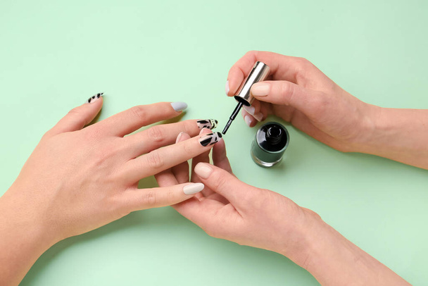 Manicure master applying polish onto press-on nail on green background, closeup - Photo, Image