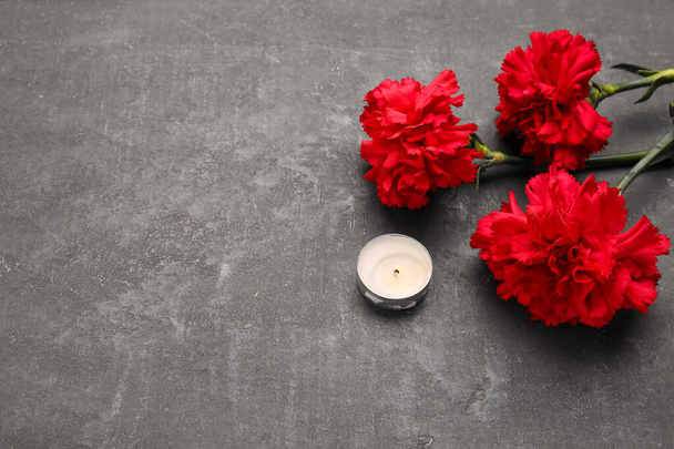 Red carnations and candle on dark grunge background - Foto, Imagen